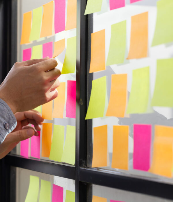 IT worker tracking his tasks on kanban board. Using task control of agile development methodology. Man attaching sticky note to scrum task board in the office IT worker tracking his tasks on kanban board. Using task control of agile development methodology. Man attaching sticky note to scrum task board in the office
